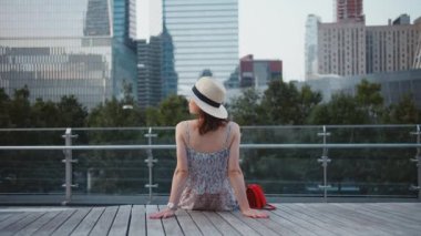 Gökdelenlerin arka planında bir bankta genç kız