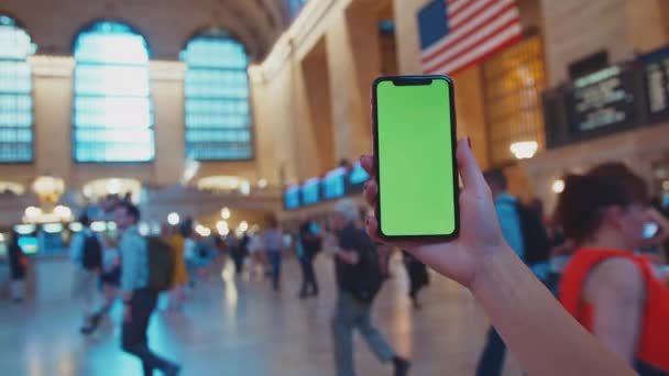 グランドセントラルターミナルに緑のディスプレイ付きスマートフォンを持つ女性の手 — ストック動画