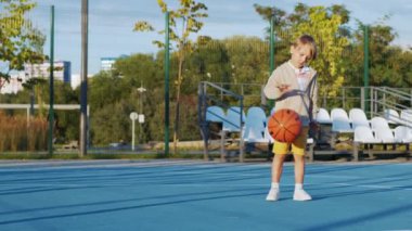 Küçük çocuk sokakta basketbol oynuyor.