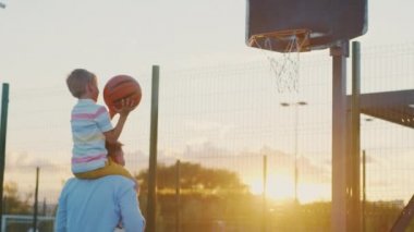Baba ve oğul gün batımında sahada basketbol oynuyorlar.