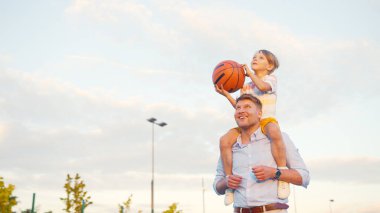 Genç adam ve çocuk yazın sahada basketbol oynuyorlar.