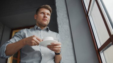 Pencerenin yanında bir fincan kahvesi olan genç bir işadamı.