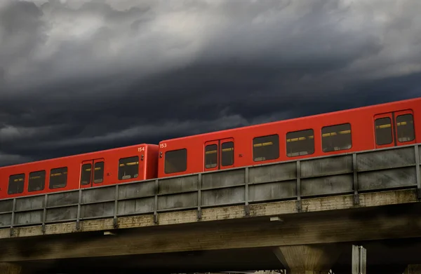 Vagones rojos del metro en un paso elevado de hormigón contra un cielo dramático —  Fotos de Stock