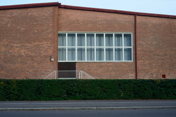 Facade of a public brick building with a large window, deadpan photo