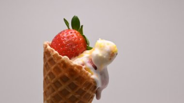 Waffle külahında lezzetli vanilyalı dondurma topları taze çileklerle erir ve beyaz arka planda akar. 