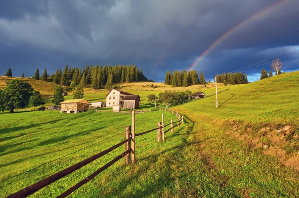 A farm house in a green sunny field and a rainbow.