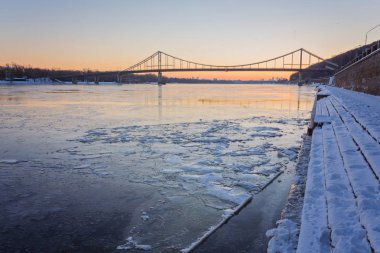 Ukrayna, Kiev 'de aydınlatılmış binaları olan soğuk kış gecesi şehirleri. Donmuş Dinyeper nehri ön planda beliriyor.