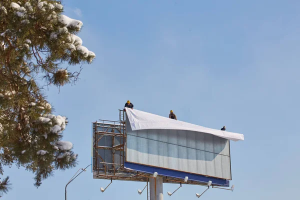 Çalışan billboard yeni reklam yükleme için hazırlar. Bir merdiven çalışma - bir reklam banner yerleştirerek endüstriyel dağcı.