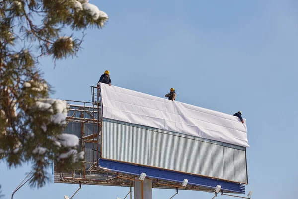 Çalışan billboard yeni reklam yükleme için hazırlar. Bir merdiven çalışma - bir reklam banner yerleştirerek endüstriyel dağcı.