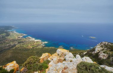 Taşlar ve kayalar krem ile ön plana içinde süzülüyor ve Polis kumsalda, Kıbrıs akan sörf. Arka plan daha fazla kıyı ve ufukta Troodos Dağları içerir.