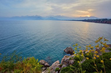 Antalya, Türkiye'de açık günbatımı gökyüzü yüksek dağlardan deniz manzarası timelapse. Deniz ve ön plan çiçekler.