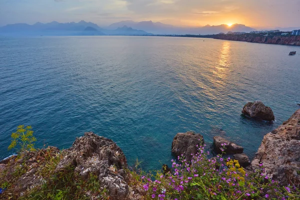 Antalya, Türkiye'de açık günbatımı gökyüzü yüksek dağlardan deniz manzarası timelapse. Deniz ve ön plan çiçekler.