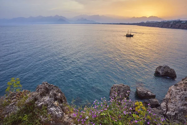 Antalya, Türkiye'de açık günbatımı gökyüzü yüksek dağlardan deniz manzarası timelapse. Deniz ve ön plan çiçekler.