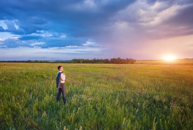 İşadamı alan görkemli akşam gökyüzü ile bir ayar güneş altında mesafe bakarak onun omuz ayakta üzerinde asılı ceketi ile şık elbiseli.