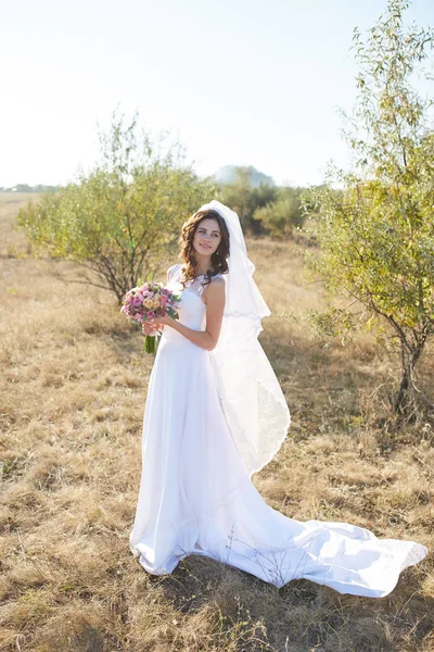 Beautiful smiling bride wearing a natural flower wreath and standing in the golden summer fields with eucalyptus in hands.