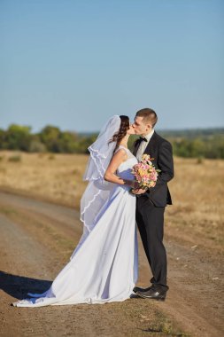 Şık gelin ve damat düğün günü dışarıda birlikte poz veriyorlar.