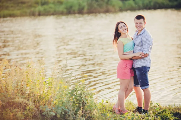 情人在湖中。这对恋爱中的年轻夫妇坐在水边的公园里，而这对年轻夫妇则在日落时弹吉他. — 图库照片