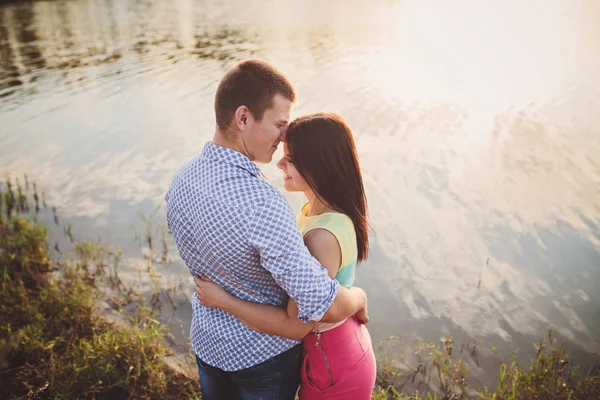 Amantes en un lago. Pareja joven enamorada sentada en el suelo del parque cerca del agua mientras estos jóvenes tocan la guitarra al atardecer. — Foto de Stock