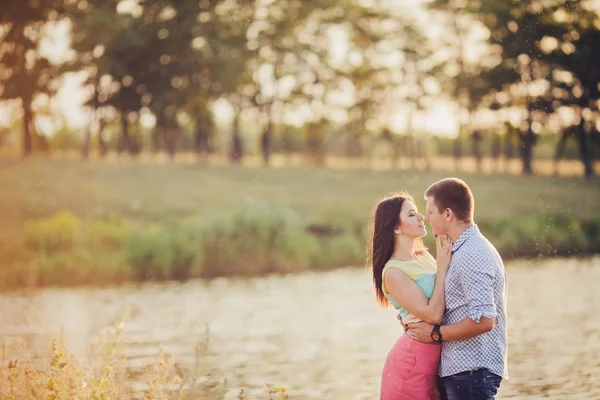 Amantes en un lago. Pareja joven enamorada sentada en el suelo del parque cerca del agua mientras estos jóvenes tocan la guitarra al atardecer. —  Fotos de Stock