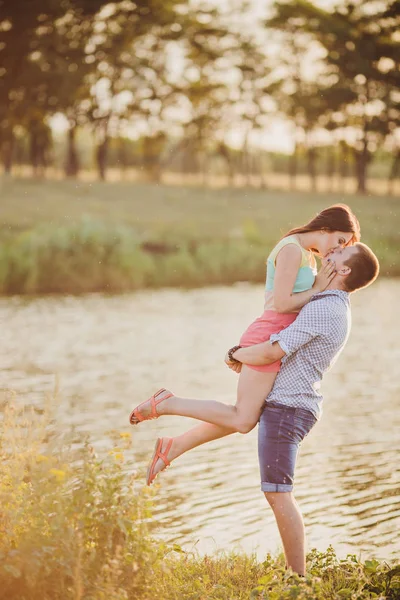 Amantes en un lago. Pareja joven enamorada sentada en el suelo del parque cerca del agua mientras estos jóvenes tocan la guitarra al atardecer. — Foto de Stock