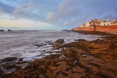 Atlantik Okyanusu dalgaları dramatik günbatımı gökyüzü ile Essaouira Fas şehir surlarının altında