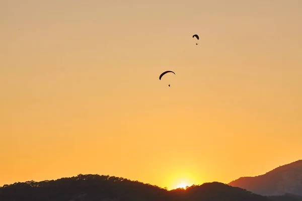 Paraglider silhouette flying over misty mountain valley in beautiful warm sunset colors - sport, active wallpapers full of freedom. Background with space for your montage