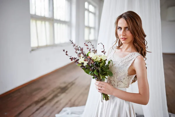 Bela noiva em um vestido de noiva em um estúdio elegante brilhante. Casamento em estilo europeu. Decoração e buquê na mão . — Fotografia de Stock