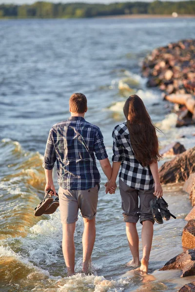 young couple in plaid shirts walking along the shore of the lake