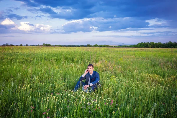 Empresário sentado em seu terno em um campo ensolarado verde telefonando f — Fotografia de Stock