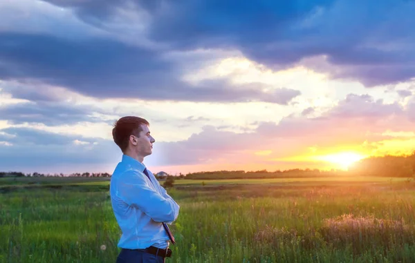 Podnikatel, stojící na poli před západem slunce — Stock fotografie