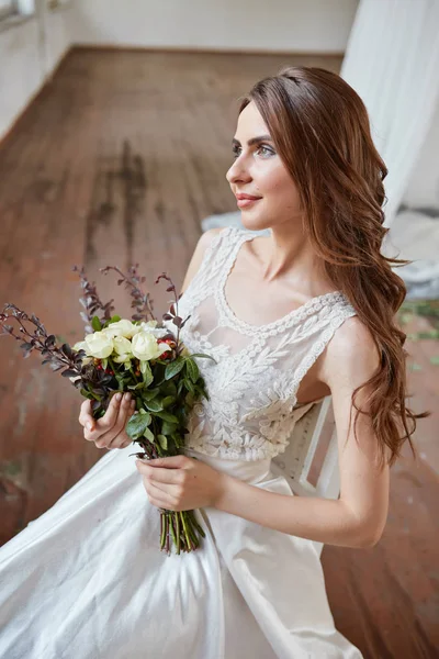 Όμορφη νύφη σε ένα νυφικό σε ένα φωτεινό κομψό στούντιο. Γάμος σε ευρωπαϊκό στιλ. Διακόσμηση και ανθοδέσμη στο χέρι. — Φωτογραφία Αρχείου