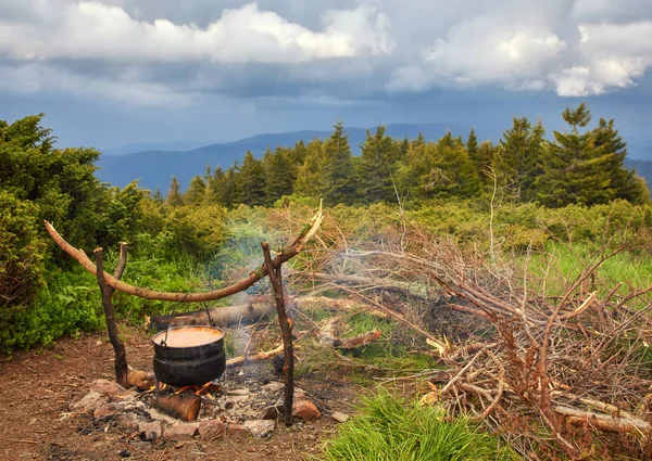Chaleira pequena velha é aquecida em uma fogueira em um prado de montanha verde durante um mau tempo . — Fotografia de Stock