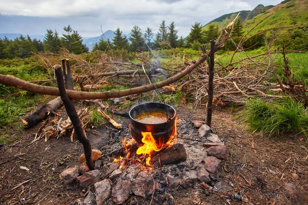 Chaleira pequena velha é aquecida em uma fogueira em um prado de montanha verde durante um mau tempo . — Fotografia de Stock