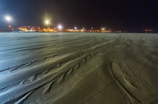 El agua retrocede en la marea baja con líneas texturizadas en la arena y la luz solar de la noche reflejándose a lo largo de los bordes . —  Fotos de Stock