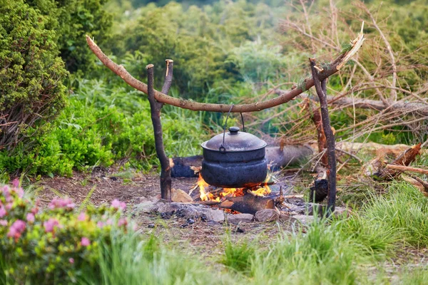 Old small kettle is heated on a bonfire on a green mountain meadow during a bad weather.