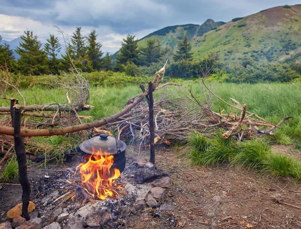 Old small kettle is heated on a bonfire on a green mountain meadow during a bad weather. — Stock Photo, Image
