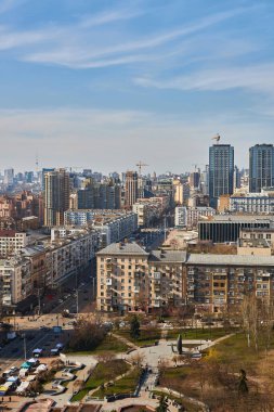 A bustling tree-lined boulevard in modern Kyiv on a sunny day, with cars in traffic, pedestrians on sidewalks, and contemporary buildings in the background.