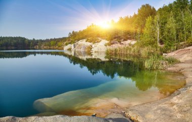 Korostyshiv, Ukrayna yakınlarındaki temiz su ocağı gölü, kayalık kıyılar, uçurumlar ve etrafındaki ormanın yansımaları yer alıyor..