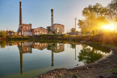 Tanınmış bacaları ve çürüyen binaları olan eski, terk edilmiş bir fabrika bir göletin veya kanalın durgun sularına açıkça yansıyor. Sanayi bozulması.