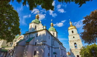 View of Saint Sophia Cathedral and Bell Tower in Kyiv on a sunny day, with people gathered in the courtyard, some seated, possibly for an event or service.