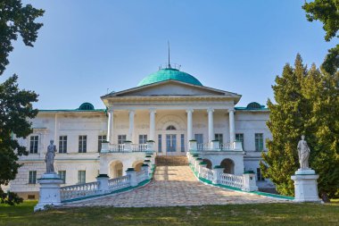 The grand classical facade of the Halagan Palace in Sokyryntsi, Ukraine, featuring a columned entrance, ramp, and statues under a clear blue sky. Historic estate.