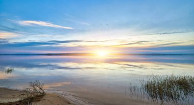 Son derece sakin bir göl alacakaranlıkta akşam gökyüzünün canlı ama yumuşak renklerini mükemmel bir şekilde yansıtır. Karanlık, uzak bir ağaç hattı silueti parlayan ufukta.