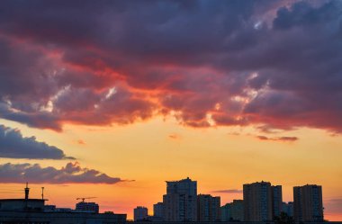 Şehir siluetinin dramatik silueti, inşaat vinçleri de dahil, turuncu, pembe ve mor bulutlardan oluşan canlı bir günbatımı gökyüzüne karşı, durgun suya yansıyor..