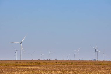 Açık mavi gökyüzünün altında bir rüzgar türbini tarlası. Yenilenebilir enerji ve sürdürülebilir güç üretim kavramı.