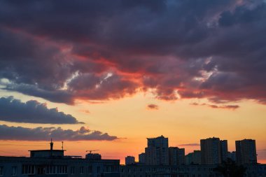 Şehir siluetinin dramatik silueti, inşaat vinçleri de dahil, turuncu, pembe ve mor bulutlardan oluşan canlı bir günbatımı gökyüzüne karşı, durgun suya yansıyor..