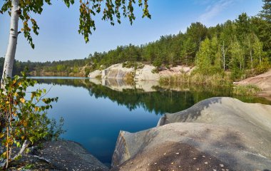 Korostyshiv, Ukrayna yakınlarındaki temiz su ocağı gölü, kayalık kıyılar, uçurumlar ve etrafındaki ormanın yansımaları yer alıyor..