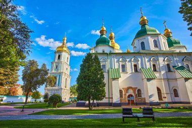 Saint Sophia Cathedral and its Bell Tower in Kyiv, a historic Orthodox complex with white walls, green and golden domes, under a blue summer sky. UNESCO site.