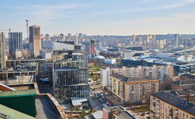 A bustling tree-lined boulevard in modern Kyiv on a sunny day, with cars in traffic, pedestrians on sidewalks, and contemporary buildings in the background.