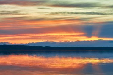 Sakin bir göl, derin mavi ve mor gökyüzünün alacakaranlığının son soluk ışığını yansıtır. Karanlık, siluetli bir ağaç çizgisi uzak ufku işaret ediyor. Huzurlu gece karanlığı sahnesi.