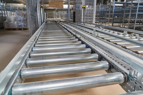 Detailed close-up view of a robust industrial roller conveyor system with metallic rollers, designed for automated material or package handling in a warehouse or factory.